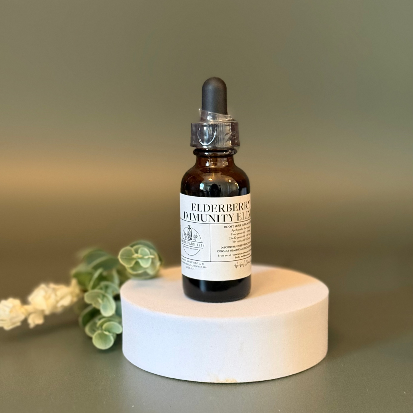 Bottle of Elderberry Immunity Tonic on a white stand with a blurred green background