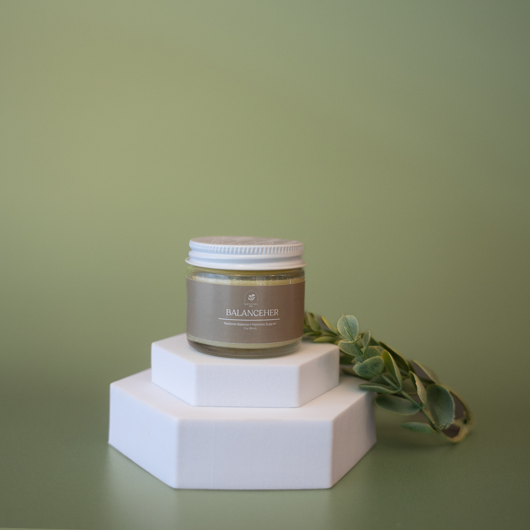 Jar of cream on a white hexagonal stand with green leaves against a green background