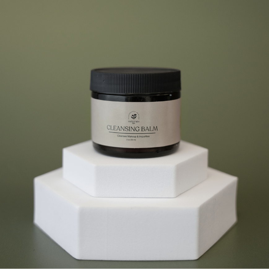 Cleansing balm jar on a white hexagonal stand against a green background