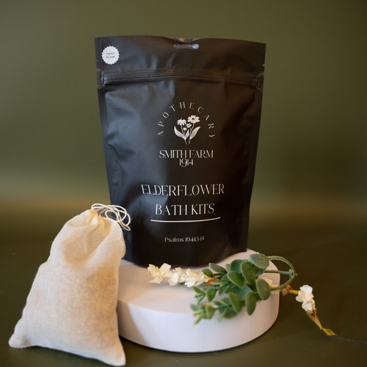 Black bath kit packaging with a white pouch and greenery on a dark background