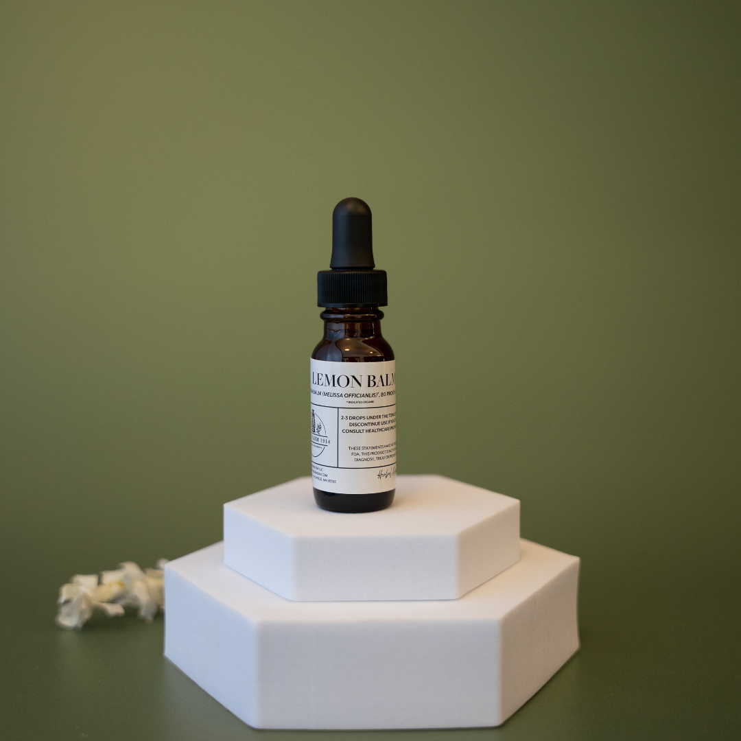 Bottle of lemon balm tincture on a white hexagonal stand against a green background